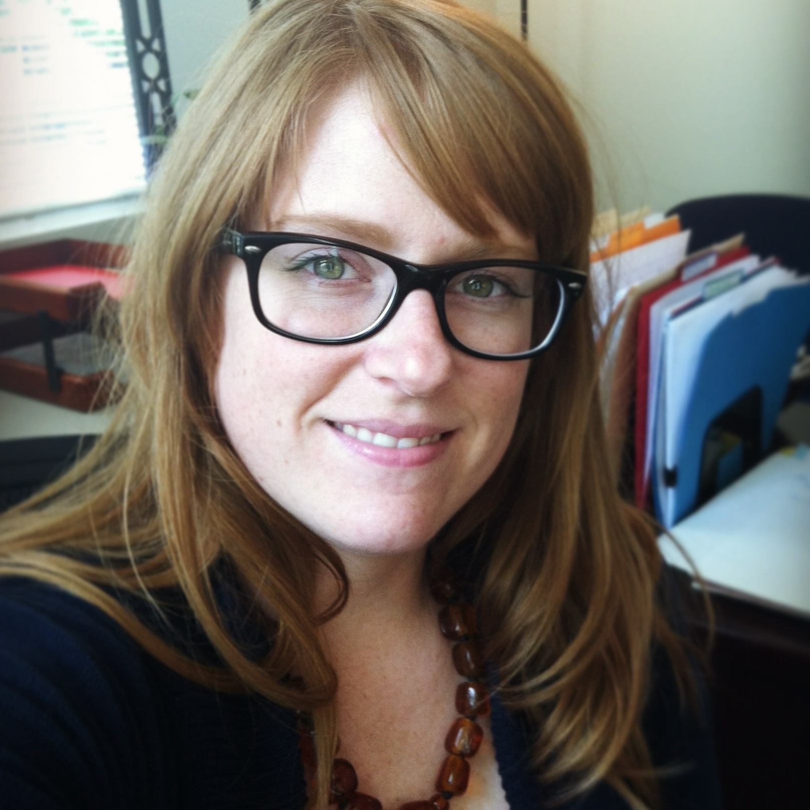 Alison Walsh smiles at the camera. She is wearing glasses with black frames, and her bangs are swept to the side.