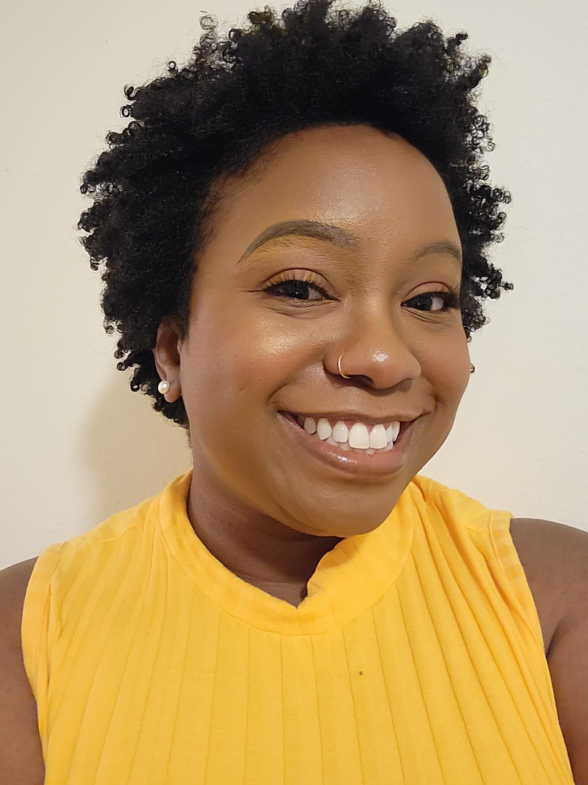 Kimberly is wearing a yellow shirt and smiling against a with a white background.
