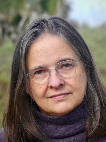 A headshot of Susan Hegeman taken outdoors. She is wearing a turtleneck sweater and silver glasses.