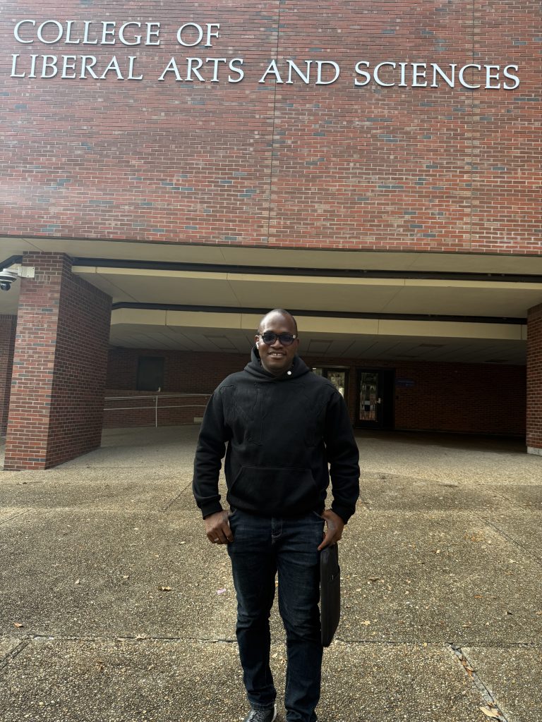 Christopher Ezeonu wearing a hoody and smiling at the camera in front of Turlington Hall at UF