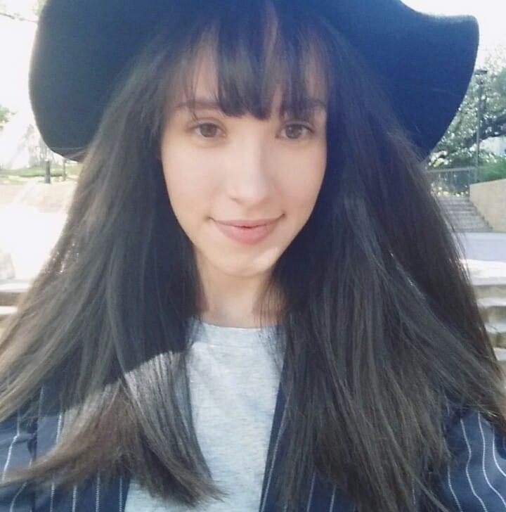 Lillian Marie Martinez is smiling. She is wearing a black hat and a striped, blue blazer.