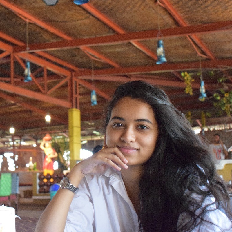 Annesha Palit sits, resting her chin on her hand. She is smiling at the camera.