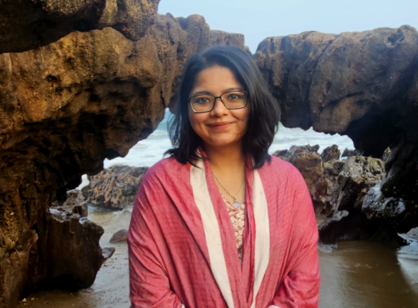 Kajori smiles at the camera. She is dressed in a traditional shawl. The picture is taken in front of the natural rock arch near Rushikonda beach.