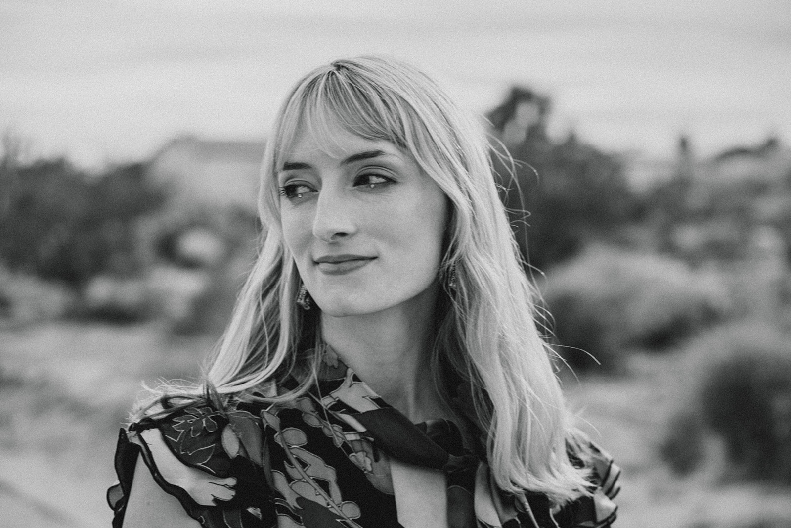 A black and white portrait of Sophie McHugh, a blond woman, looking off camera and smirking.