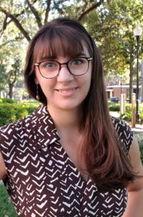 A white woman with glasses wearing a brown dress smiles in front of UF’s Library West.