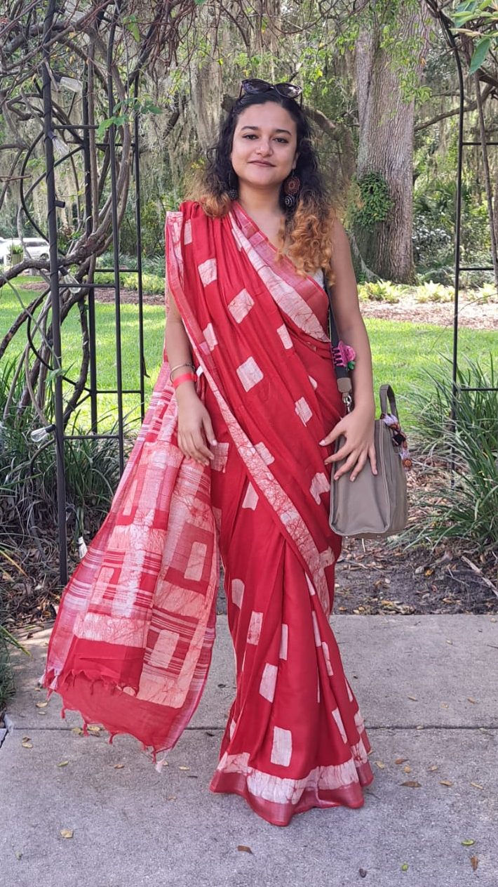 Anomitra looks at the camera. She/they are wearing a red Sari.